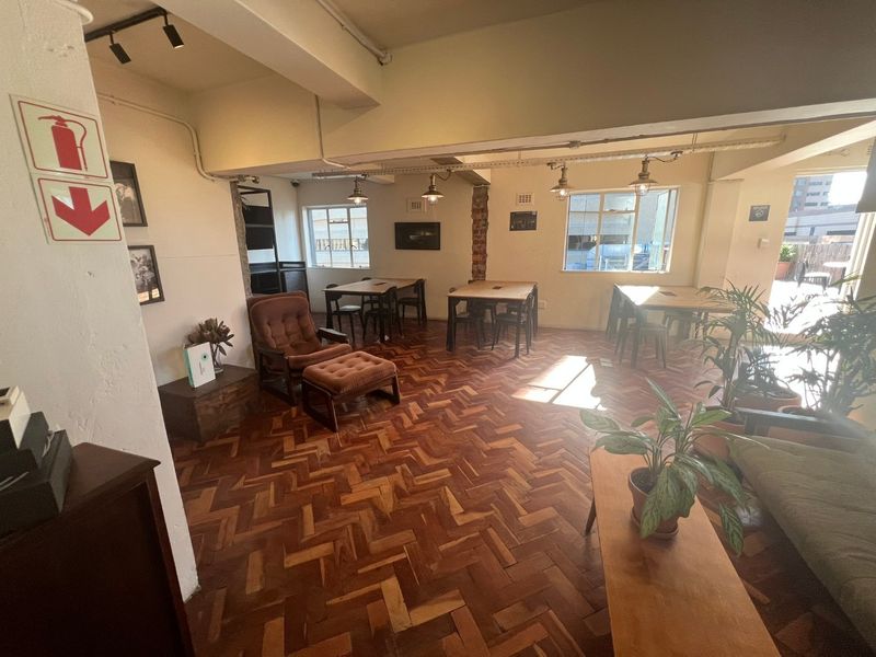 Spacious open-plan living area featuring classic herringbone parquet flooring, exposed structural beams, and industrial-style lighting, offering a versatile layout with abundant natural light.