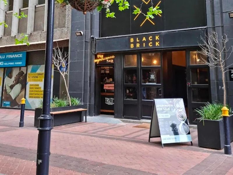 Street-level view of the Black Brick apartment building entrance featuring a modern storefront facade and paved pedestrian access.