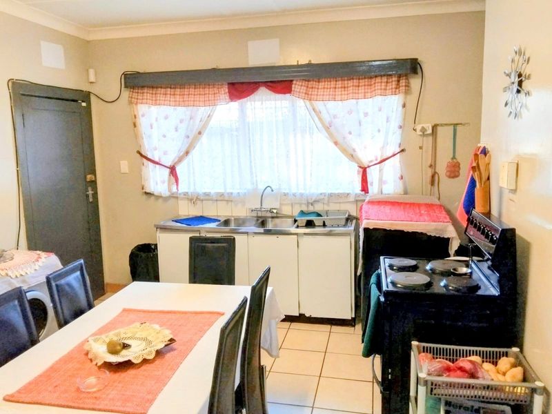 A functional kitchen area featuring tiled flooring, a stainless steel sink, and a freestanding stove, offering potential for modernization and layout optimization.