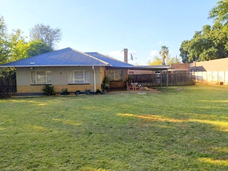 Rear view of the house featuring a large lawn, a covered patio area, and a corrugated metal roof.