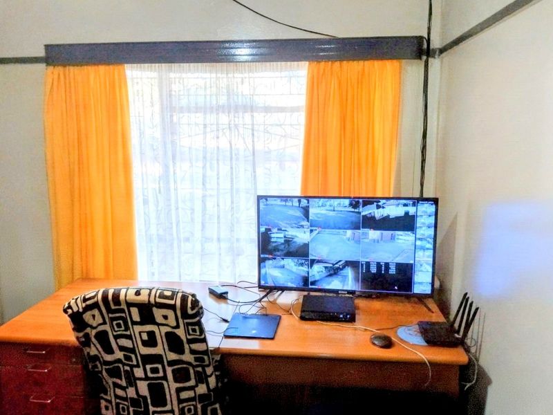 A home office space featuring a security camera monitoring system and window security bars.