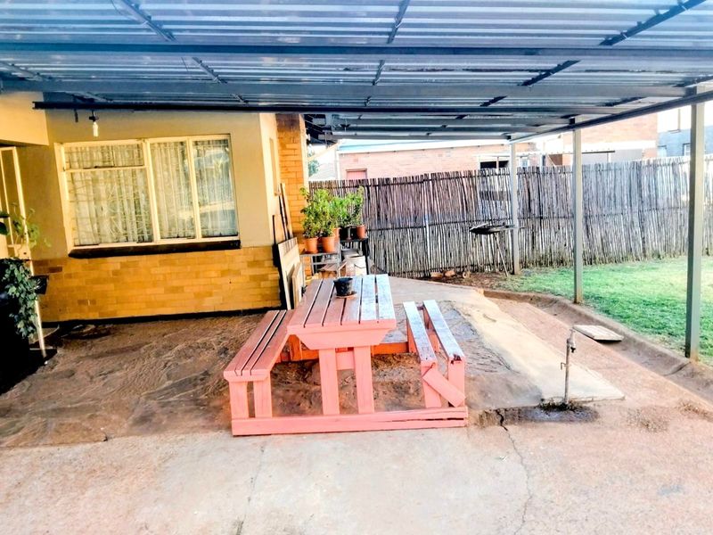 A covered outdoor patio area featuring concrete paving, a corrugated metal roof, and an external water tap, providing a functional space for outdoor living.