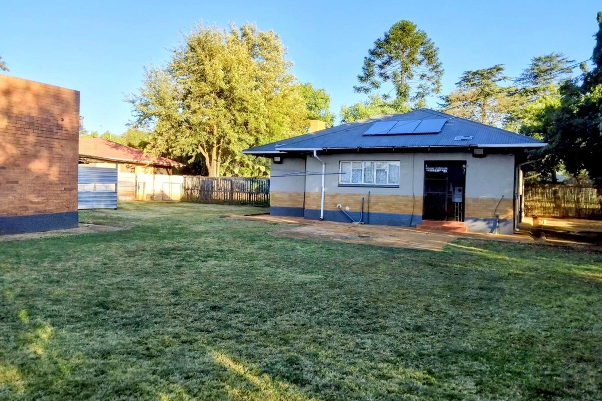 Rear view of the property featuring a spacious lawn, solar water heating panels on the roof, and a brick and plaster exterior finish.