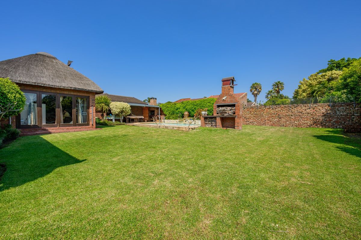 Spacious rear garden featuring a swimming pool, built-in brick braai, and a thatched-roof structure with a covered patio area.