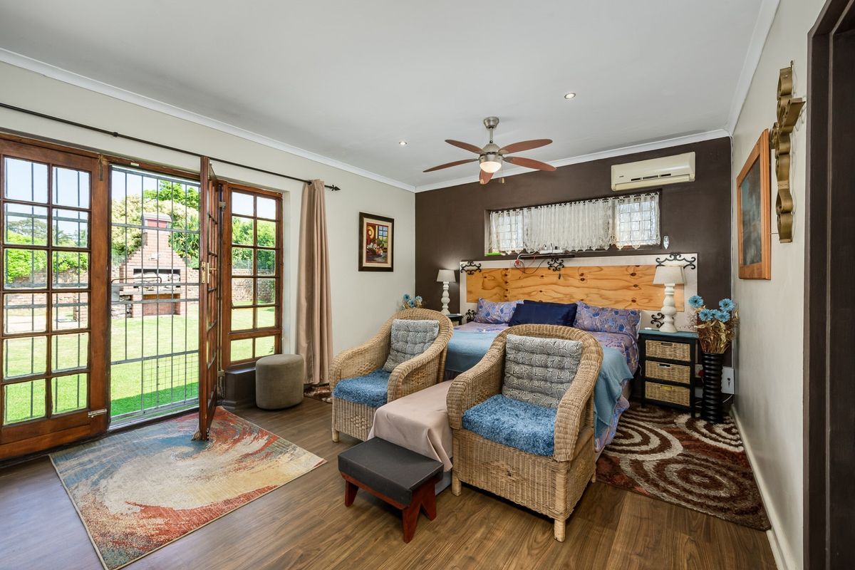 Spacious bedroom featuring laminate flooring, a ceiling fan, split-system air conditioning, and direct access to the garden through wooden french doors.