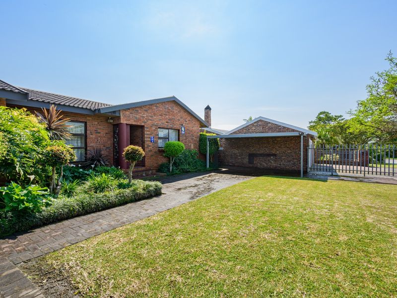 Front view of a brick house featuring a paved driveway, attached carport, and well-maintained garden area.