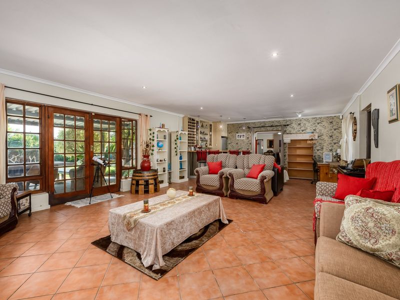 Spacious open-plan living area featuring terracotta floor tiles, recessed lighting, and large wooden-framed glass doors providing direct access to the outdoor patio area.