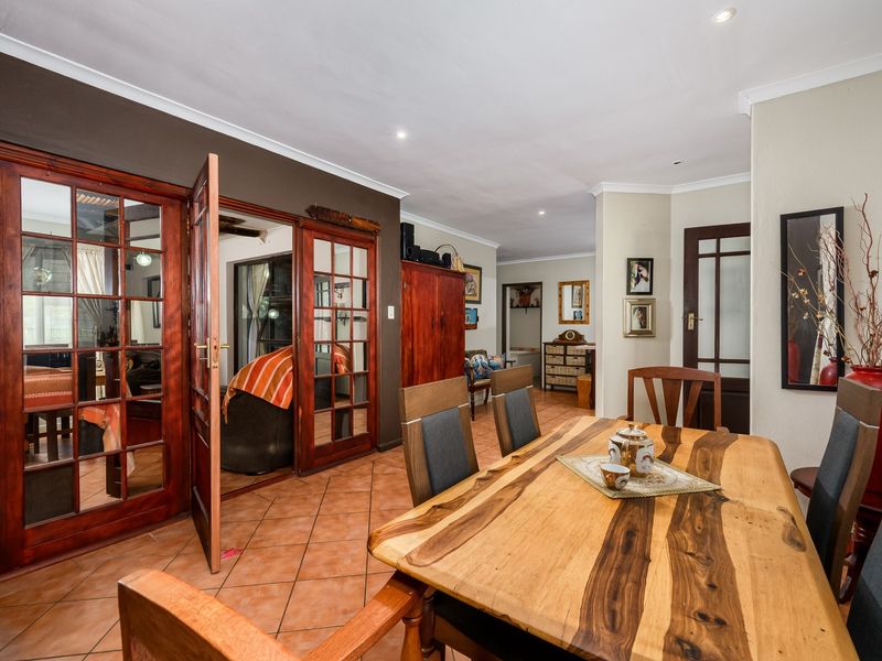 Dining area featuring terracotta floor tiles, recessed downlighting, and wooden french doors leading to an adjacent living space.