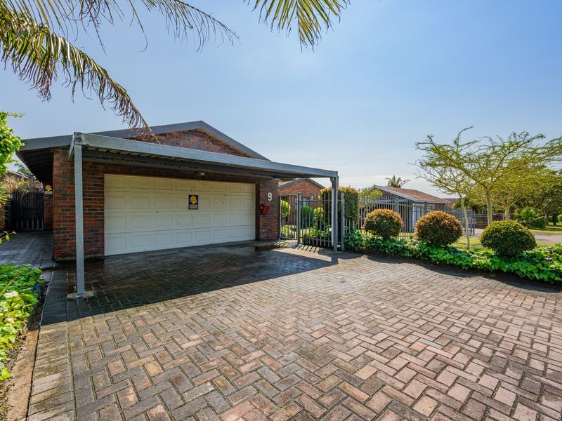 Front exterior view of the property featuring a brick facade, a covered carport, and a paved driveway with secure perimeter fencing.