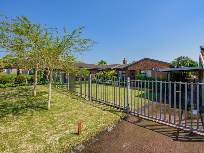 Front view of a brick house featuring a paved driveway, carport, and secure metal fencing surrounding a well-maintained lawn.