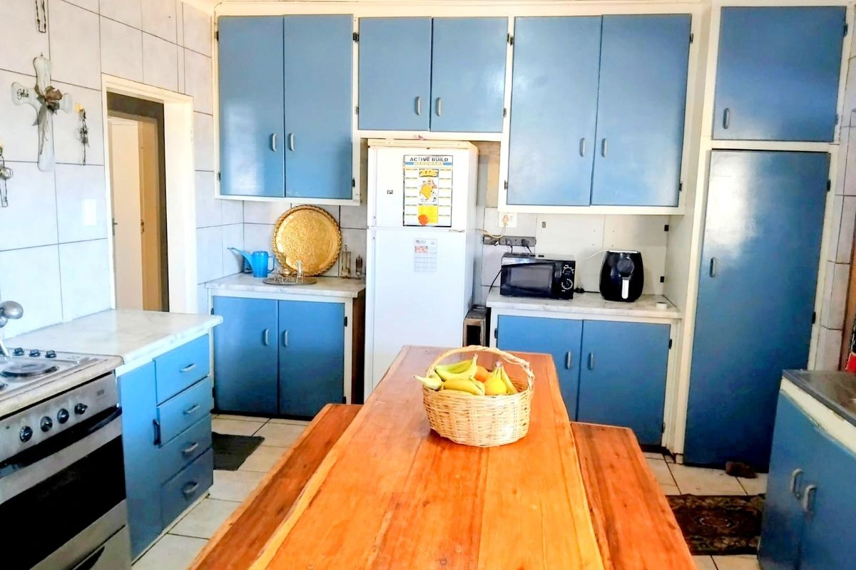 A functional kitchen featuring blue built-in cabinetry, tiled splashbacks, and a central wooden dining area, offering a dated but practical layout.