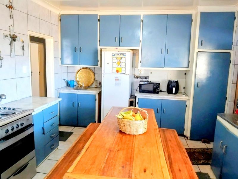 A functional kitchen featuring blue built-in cabinetry, tiled splashbacks, and a central wooden dining area, offering a dated but practical layout.