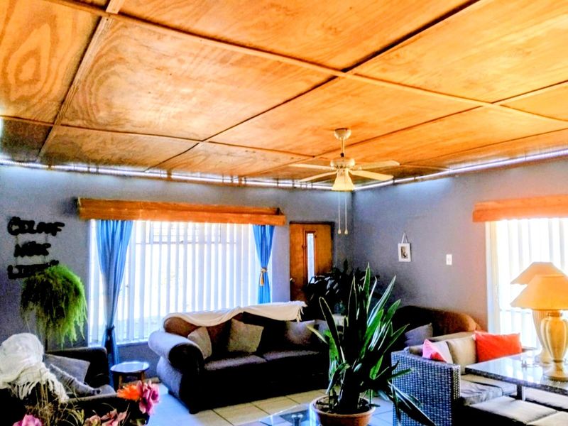 Living room featuring a plywood panel ceiling, ceiling fan, and tiled flooring with vertical blinds on the windows.