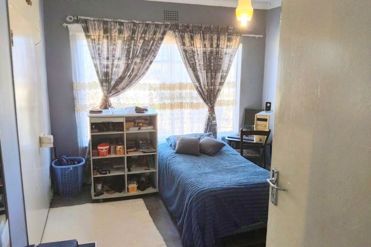 A functional bedroom featuring a window with curtains, a built-in cupboard, and a ceiling light fixture.