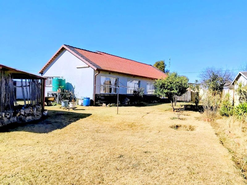 Rear view of the house featuring a tiled roof, metal window frames, and a large garden area with a water storage tank.