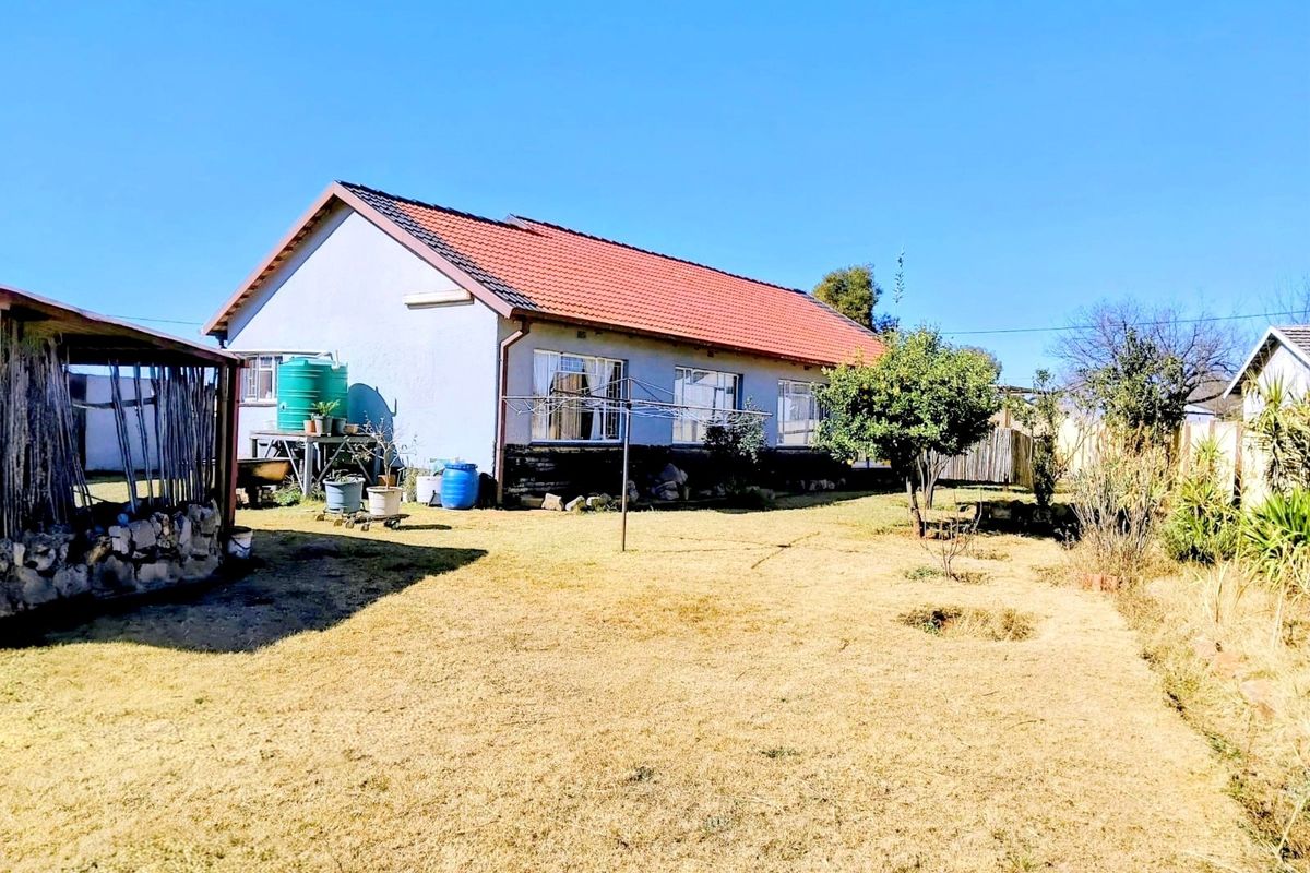 Rear view of the house featuring a tiled roof, metal window frames, and a large garden area with a water storage tank.