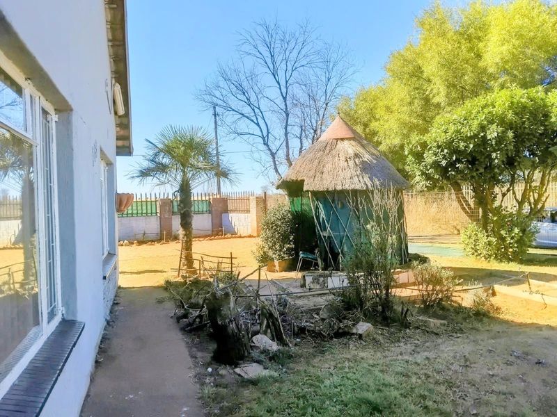 Rear garden area featuring a traditional thatched lapa, perimeter walling, and established trees, offering potential for landscaping and outdoor entertainment development.