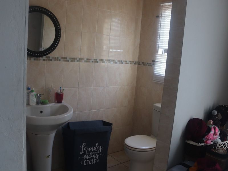 A functional bathroom featuring a pedestal basin, toilet, and neutral ceramic wall tiling with a decorative mosaic accent border.