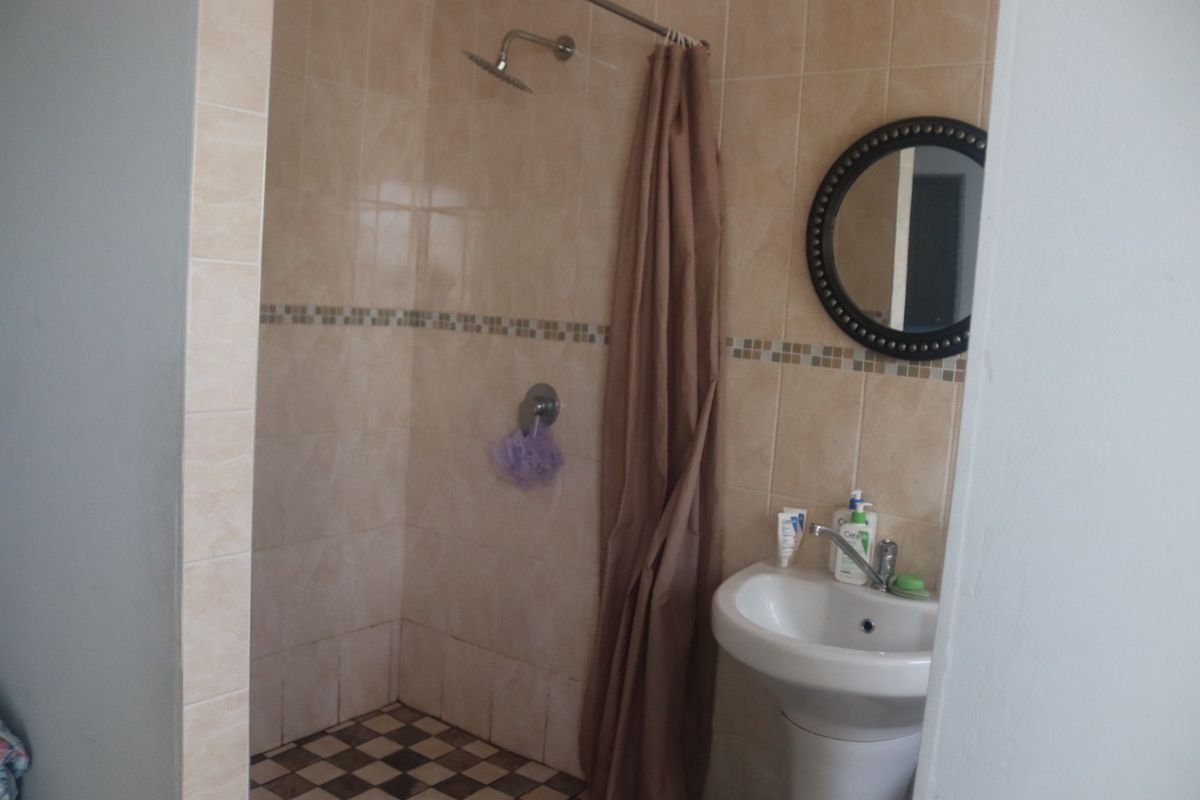 A functional bathroom featuring a shower enclosure with tiled walls, a mosaic border, and a pedestal basin with a mixer tap.