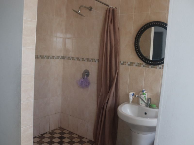 A functional bathroom featuring a shower enclosure with tiled walls, a mosaic border, and a pedestal basin with a mixer tap.