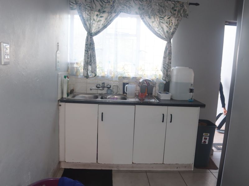 A compact kitchen area featuring a double sink, tiled splashback, and basic built-in base cabinetry with a laminate countertop.