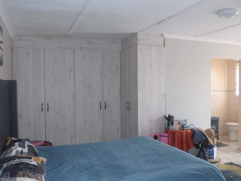 A bedroom featuring light wood-look built-in cupboards, tiled flooring, and an adjoining en-suite bathroom.