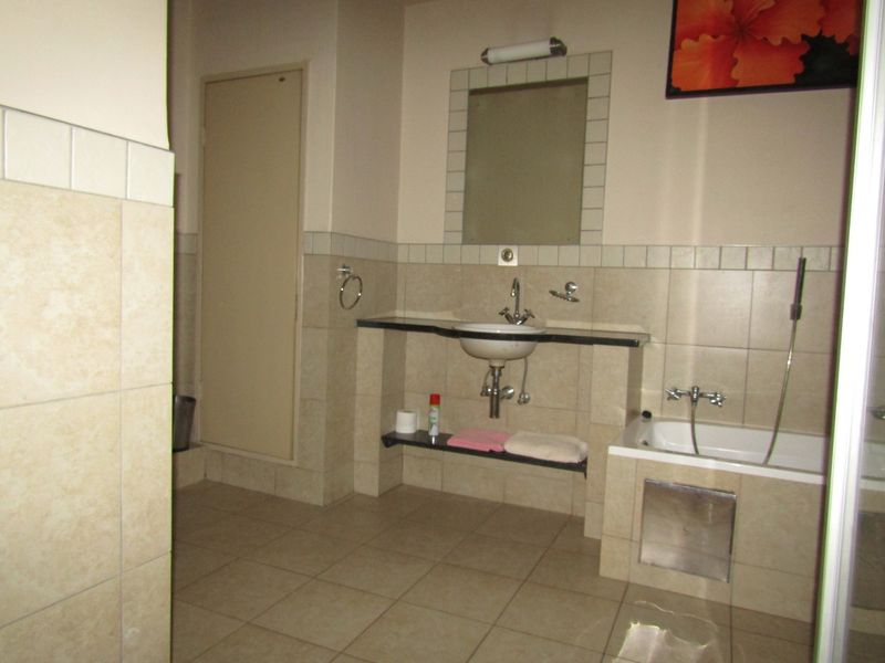 A functional bathroom featuring tiled walls and floors, a built-in vanity with a basin, and a bathtub with a handheld shower attachment.