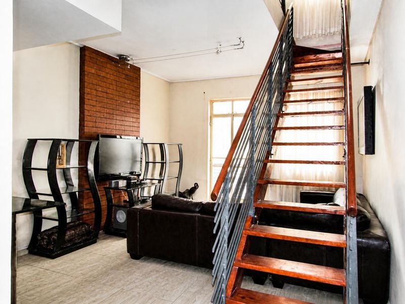 Living room featuring a brick accent wall and a prominent wooden staircase with metal balustrades, leading to an upper level.