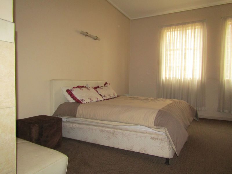 A standard bedroom featuring carpeted flooring, neutral wall tones, and natural light provided by two windows with curtains.