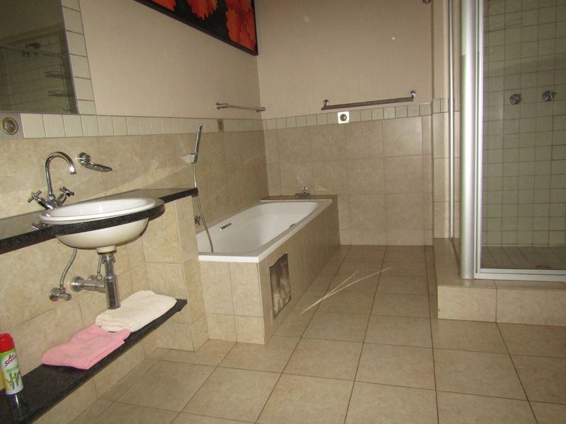 A functional bathroom featuring a built-in bathtub, a separate shower enclosure, and a wall-mounted basin with neutral tiled finishes throughout.