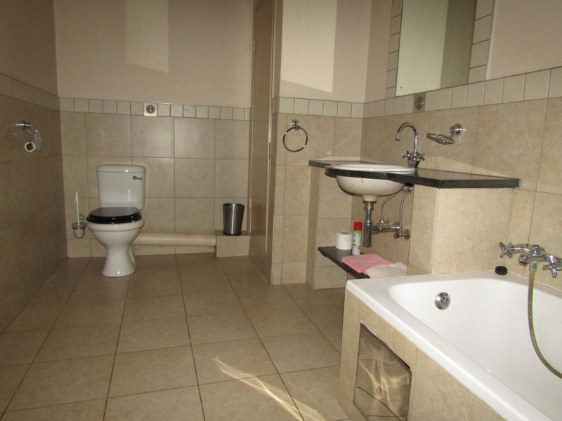 A functional bathroom featuring a bathtub, toilet, and wall-mounted washbasin with tiled finishes throughout.