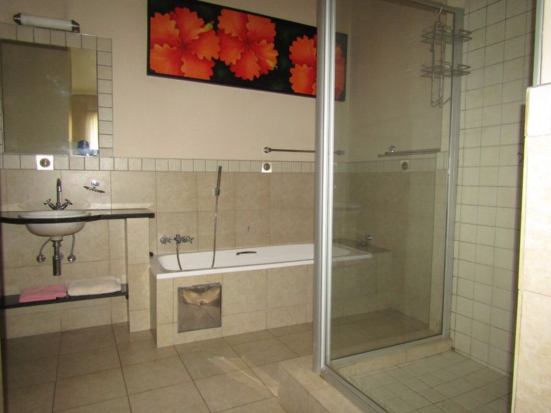 A functional bathroom featuring a built-in bathtub, separate glass-enclosed shower, and wall-mounted basin with tiled finishes throughout.