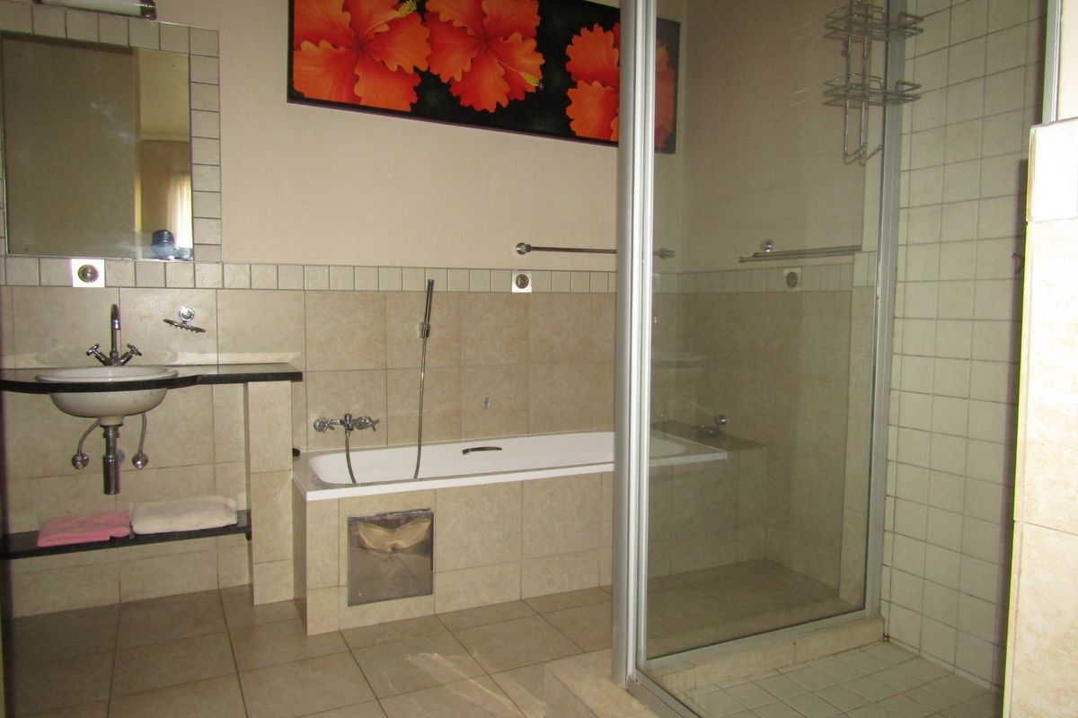 A functional bathroom featuring a built-in bathtub, separate glass-enclosed shower, and wall-mounted basin with tiled finishes throughout.