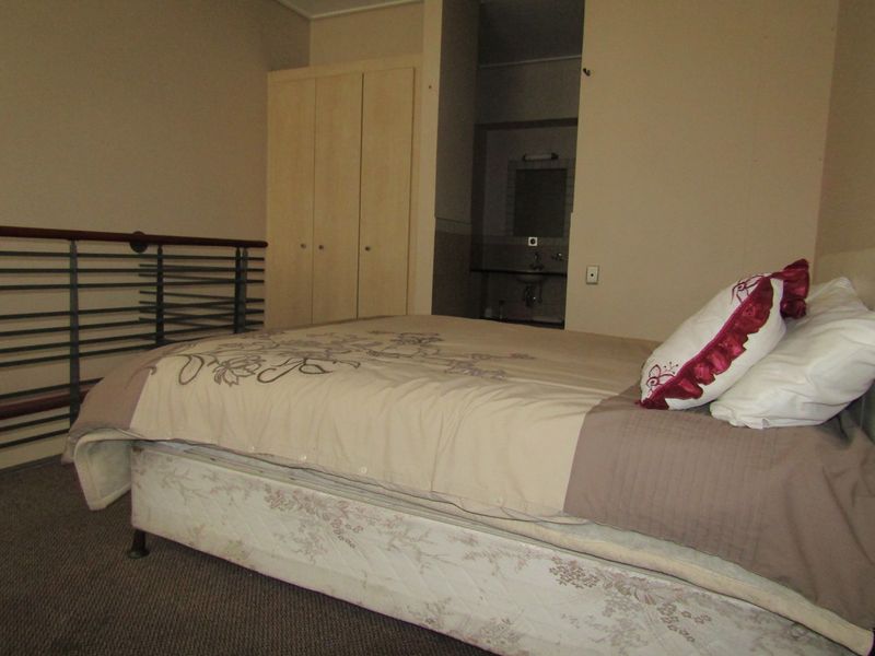 A bedroom featuring a built-in wardrobe, metal balustrade, and direct access to an en-suite bathroom.