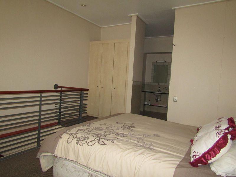 Bedroom featuring a built-in wardrobe, metal balustrade overlooking the lower level, and an open-plan en-suite vanity area.