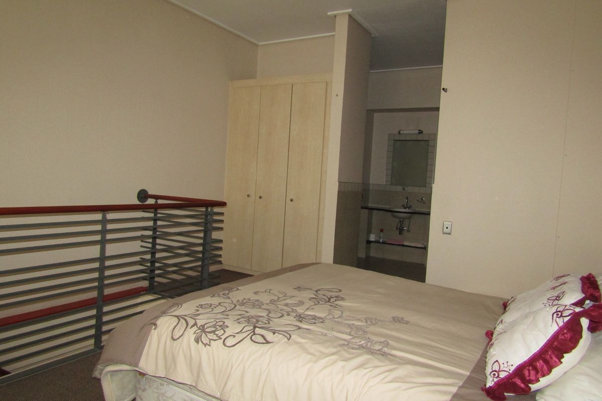 Bedroom featuring a built-in wardrobe, metal balustrade overlooking the lower level, and an open-plan en-suite vanity area.