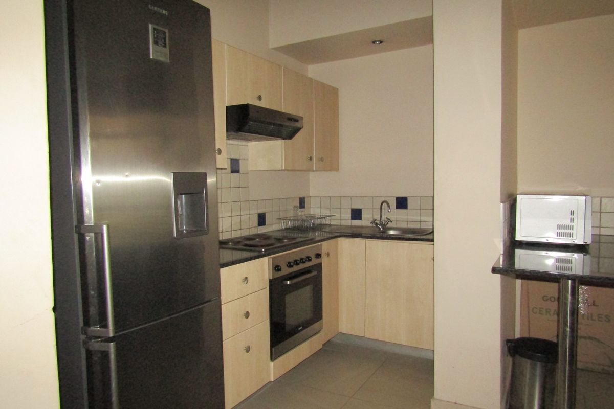 Compact kitchen featuring light wood cabinetry, granite countertops, tiled backsplash, and built-in oven with extractor fan.