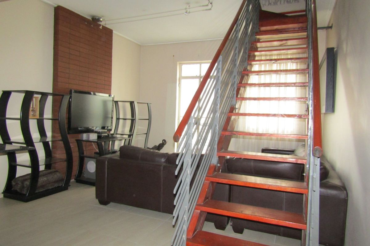 Living room featuring a brick accent wall and an open-tread staircase with a metal balustrade, finished with neutral floor tiles.