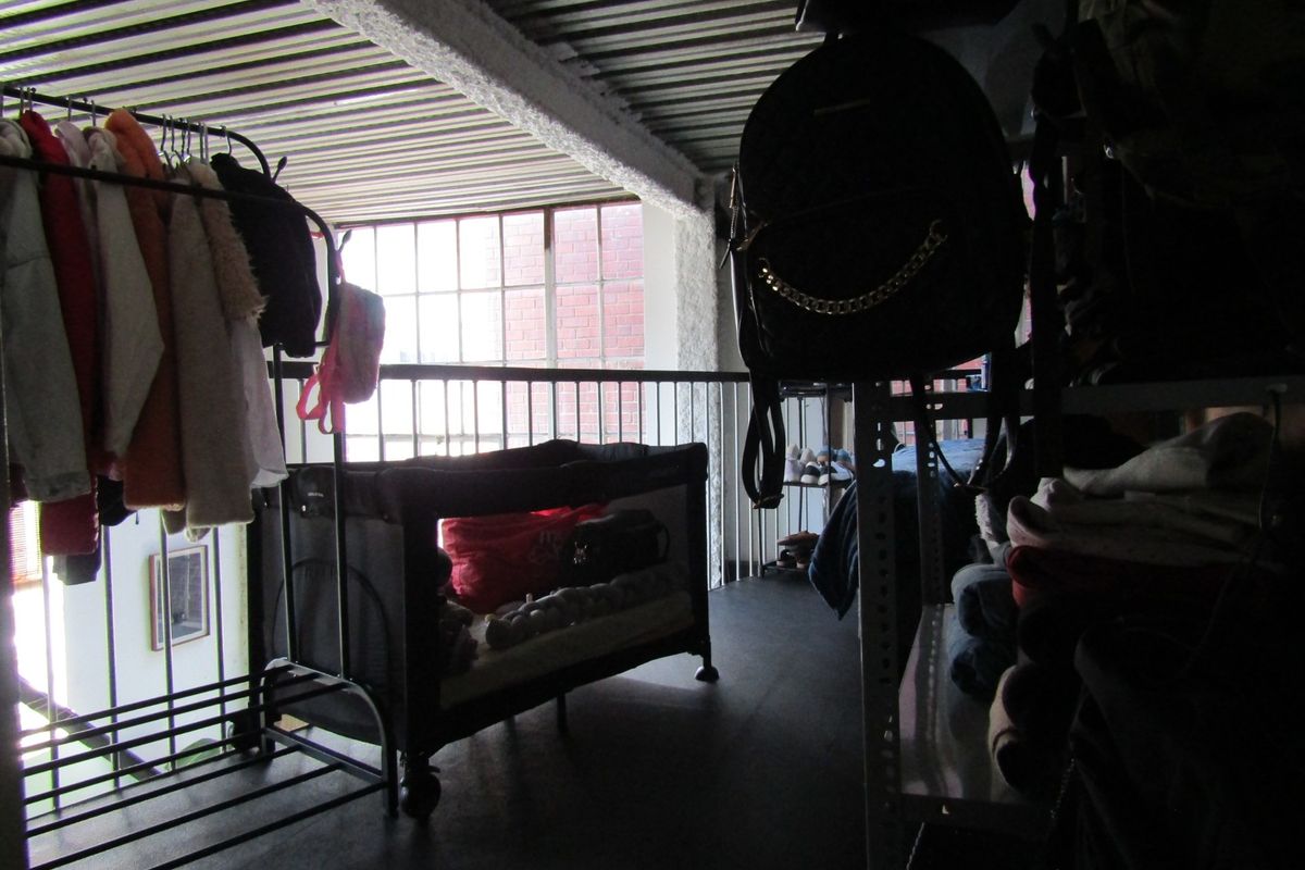 A mezzanine bedroom area featuring an industrial aesthetic with exposed corrugated metal ceilings, a metal balustrade, and a large window overlooking the lower level.