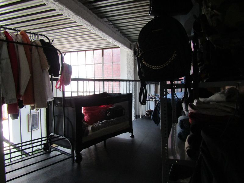 A mezzanine bedroom area featuring an industrial aesthetic with exposed corrugated metal ceilings, a metal balustrade, and a large window overlooking the lower level.