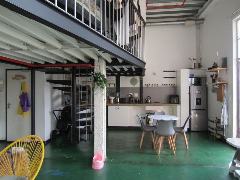 Open-plan apartment featuring an industrial aesthetic with a mezzanine level, spiral staircase, exposed ceiling elements, and a functional kitchen area.