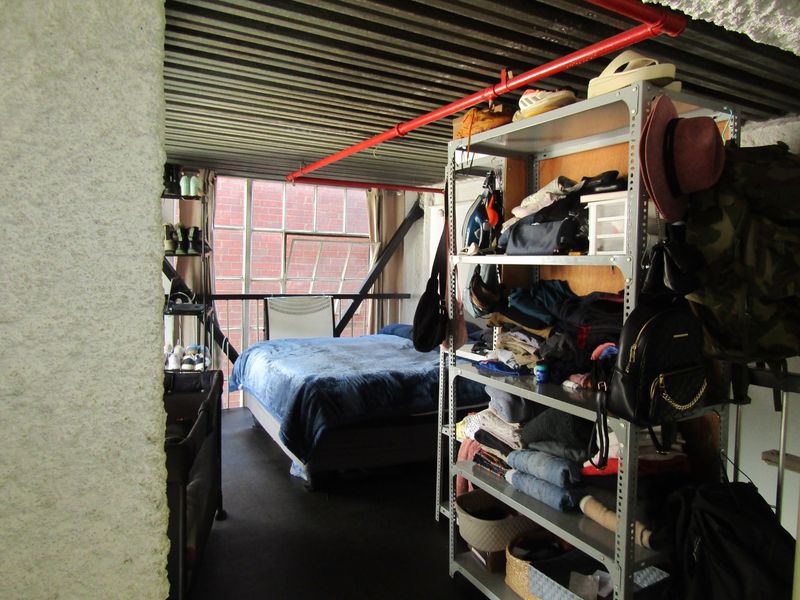 Industrial-style bedroom featuring exposed corrugated metal ceilings, red fire sprinkler piping, and large steel-framed windows with structural bracing.