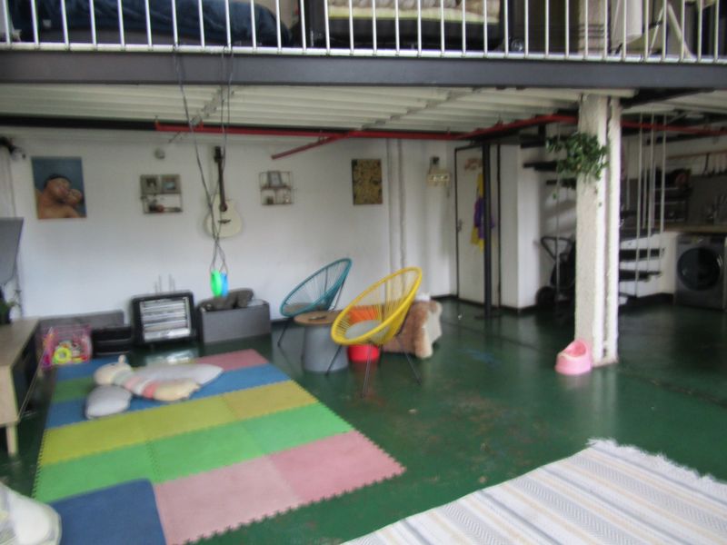 Open plan living area featuring a mezzanine level, industrial-style exposed ceiling pipes, and a painted concrete floor in an apartment setting.