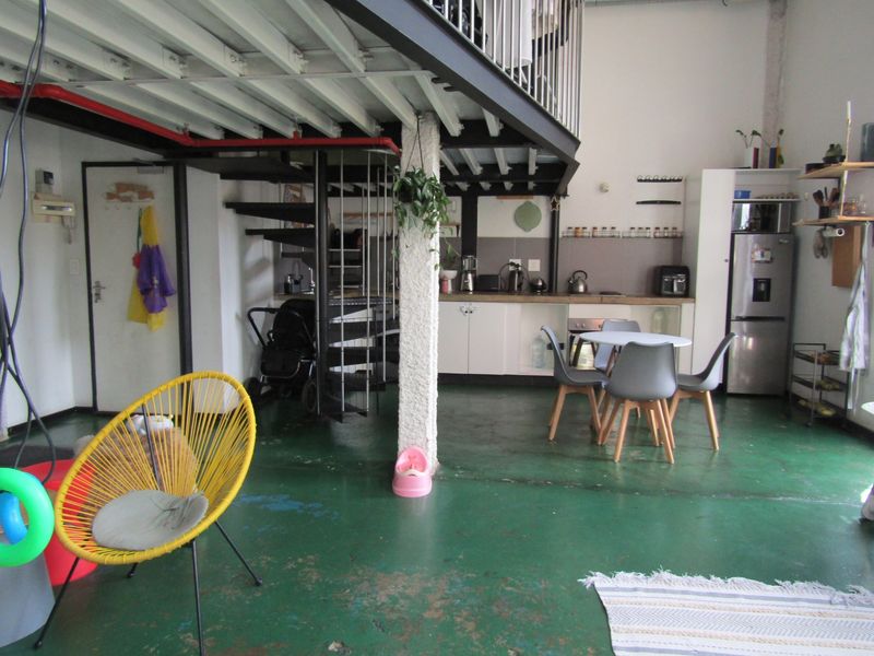 Open plan living area featuring a mezzanine level with a spiral staircase, industrial style exposed steel beams, and a functional kitchen space.