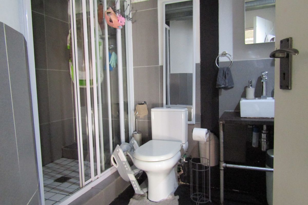 Compact bathroom featuring a shower enclosure, toilet, and vanity basin with tiled finishes. Requires minor cosmetic updates to ceiling and fixtures.