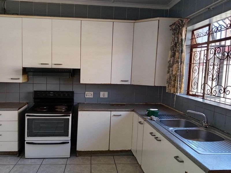 A functional kitchen featuring white cabinetry, a double bowl stainless steel sink, tiled splashbacks, and a freestanding stove with an extractor fan.