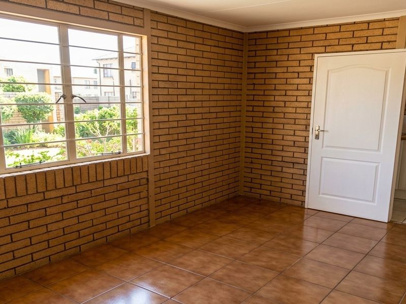 An empty living area featuring exposed brick walls, tiled flooring, and a large window with security bars, offering a clean, neutral space.