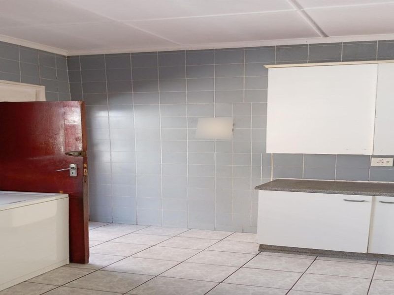 A functional kitchen area featuring tiled walls, tiled flooring, and built-in cabinetry with laminate countertops, offering a practical space for culinary activities.