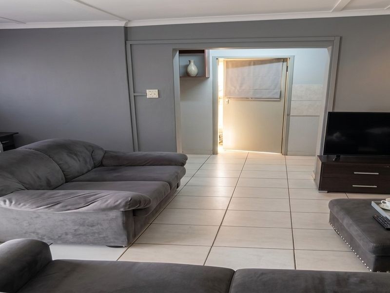 A living room featuring neutral tiled flooring and grey painted walls, with a doorway leading to an adjacent utility or secondary space.