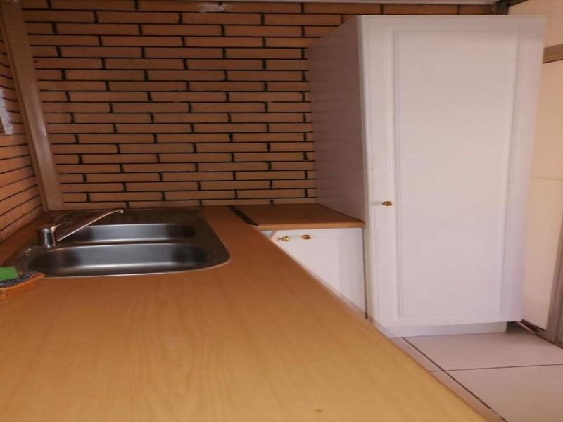 A functional scullery area featuring a stainless steel sink, laminate countertop, and built-in cabinetry against an exposed brick wall.